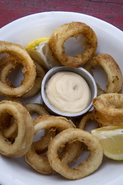 Seafood. Closeup view of fried squid rings with lemon and a dipping sauce, in a white bowl on the wooden table.