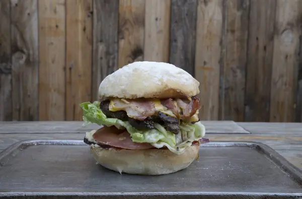View of a traditional burger with bread, bacon, cheddar cheese, lettuce and tomato.