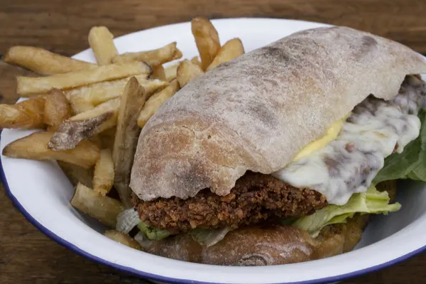 Closeup view of a chicken fried steak sandwich with lettuce, mayonnaise and french fries, in a white bowl on the wooden table.
