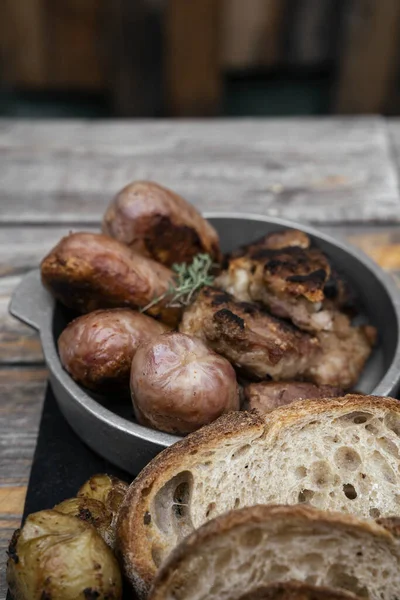 Barbekü. Geleneksel Asado Criollo tabağı. Biftek, domuz sosisi, ızgara midye, ahşap masada patates ve ekmek.. 