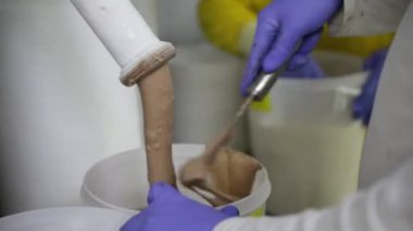 Gıda endüstrisi ve işleme. İşçilerin eldiven giydiği, ticari konteynırları endüstriyel boru sisteminden çıkan çikolatalı dondurmayla doldurduğu yakın çekim görüntüsü.