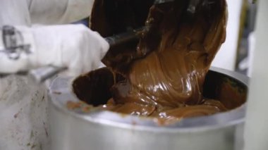 Yiyecek endüstrisi. Yakından bakınca eldiven giyen bir işçinin paslanmaz bir kaba kremalı karamel döktüğünü görüyoruz..