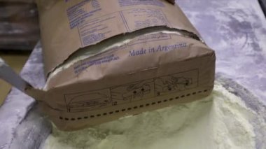 Yiyecek endüstrisi. Endüstriyel dondurma üretimi. Fabrika işçisinin vanilya esanslı bir toz torbasını keserken ve içindekileri paslanmaz bir huni makinesine boşaltırken yakın görüntüsü..