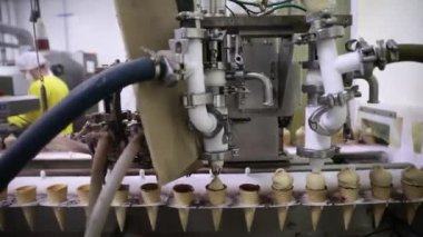 Yiyecek endüstrisi. Dondurma yapımcıları. Konileri çikolatalı dondurmayla dolduran elektrikli bir makinenin yakın görüntüsü.