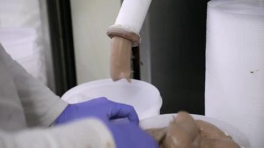 Gıda endüstrisi ve işleme. Plastik kapları çikolata dondurmasıyla dolduran işçilerin yakın görüntüsü bir borudan geliyor..
