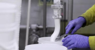 Yiyecek endüstrisi. Dondurma üretim süreci. Dondurmanın bir borudan ticari plastik bir konteynıra çıkışının yakın görüntüsü. Fabrika işçisi süreci yönetiyor..