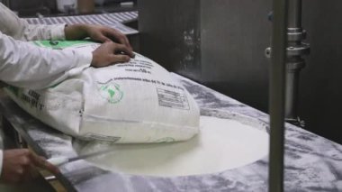 Yiyecek endüstrisi. Endüstriyel dondurma üretimi. Fabrika işçilerinin bir poşet beyaz şekeri paslanmaz huni makinesine boşalttıklarını görmek.