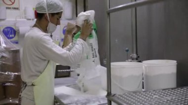 Yiyecek endüstrisi. Endüstriyel dondurma üretimi. Fabrika işçilerinin bir poşet beyaz şekeri paslanmaz huni makinesine boşalttıklarını görmek.