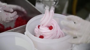 Yiyecek endüstrisi. Dondurma üretim süreci. Borudan çıkan vişne ve dondurmanın ticari plastik bir konteynıra yakın görüntüsü. Fabrika işçisi kırmızı kiraz ekliyor ve sürece rehberlik ediyor.