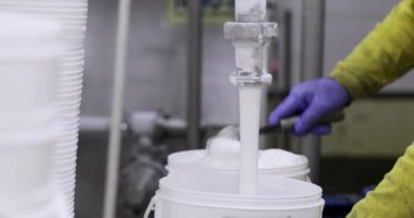 Yiyecek endüstrisi. Dondurma üretim süreci. Dondurmanın bir borudan ticari plastik bir konteynıra çıkışının yakın görüntüsü. Fabrika işçisi süreci yönetiyor..