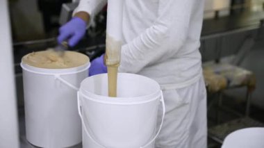 Yiyecek endüstrisi. Dondurma üretim süreci. Çikolatalı dondurmanın yakın plan görüntüsü bir borudan çıkıp ticari plastik bir kaba giriyor. Fabrika işçisi süreci yönetiyor..