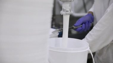 Yiyecek endüstrisi. Dondurma üretim süreci. Dondurmanın bir borudan ticari plastik bir konteynıra çıkışının yakın görüntüsü. Fabrika işçisi süreci yönetiyor..