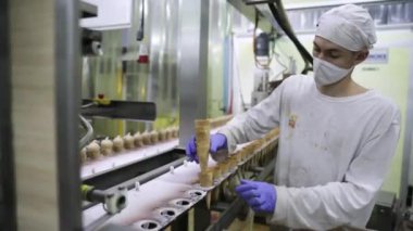 Yiyecek endüstrisi. Sanayi dondurma fabrikası. Makineye koni yerleştiren eldivenli bir operatörün yakın görüntüsü.