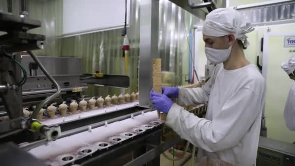 食品産業について 産業アイスクリーム工場ライン マシンにコーンを配置する手袋を持つオペレータのクローズアップビュー — ストック動画