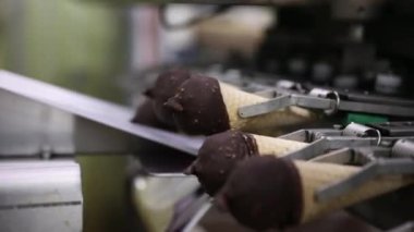 Gıda endüstrisi ve teknoloji. Ticari ambalaj makinesinin çikolata kaplı dondurma külahlarını ve plastik bir pakette fıstığı yakın plan görüntüsü..