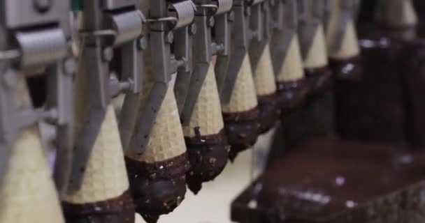 食品産業と技術について チョコレートとピーナッツでコーティングされた産業用アイスクリームコーンを輸送する工場機械のクローズアップビュー — ストック動画
