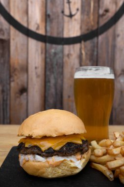 Geleneksel çizburger, çedar, soğan, patates kızartması ve bir bardak bira..