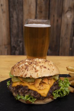 Lezzetli hamburger. Çedar peyniri, salatalık ve kızarmış domuz pastırmalı hamburger, patates kızartması ve ahşap bir arka plan.. 