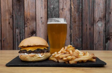 Geleneksel çizburger, çedar, soğan, patates kızartması ve bir bardak bira..
