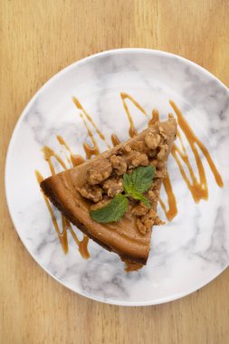 Tatlı tatlılar. Tahta arka planda beyaz mermer bir tabakta ceviz ve karamel soslu dulce de leche cheesecake diliminin üst görüntüsü.. 