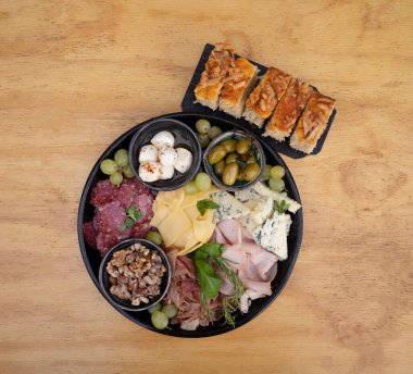 Antipasto. Dilimlenmiş salam, peynir, mavi peynir, Focaccia ekmeği, İtalyan boconccinosu, ceviz, jambon, pişirilmiş jambon ve ahşap masada yeşil zeytin..