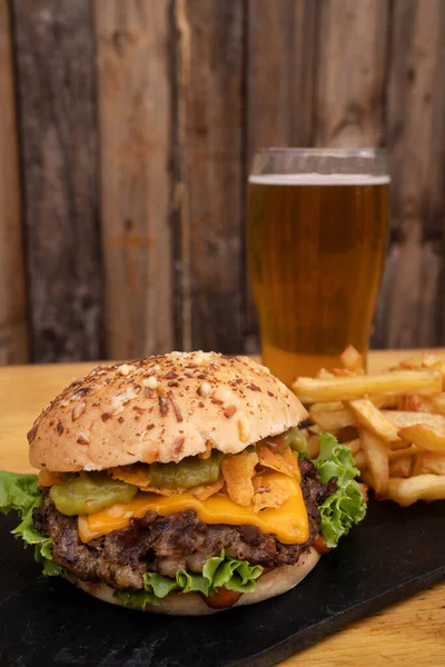 Fast food. Closeup view of a cheddar cheese and guacamole burger with a pint of beer and french fries on the wooden table.