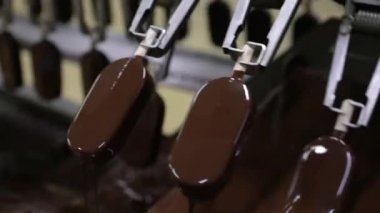 Sanayi dondurma fabrikası. Gıda üretim sektöründe otomasyon ve teknoloji. Çikolataya kremalı dondurma taşıyıp batıran bir makine görüntüsü.