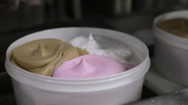 Dondurma fabrikası. Ticari dondurma tencerelerini farklı tatlarda taşıyan bir taşıma bandının yakın görüntüsü.