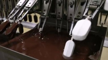 Sanayi dondurma fabrikası. Gıda üretim sektöründe otomasyon ve teknoloji. Çikolataya kremalı dondurma taşıyıp batıran bir makine görüntüsü.