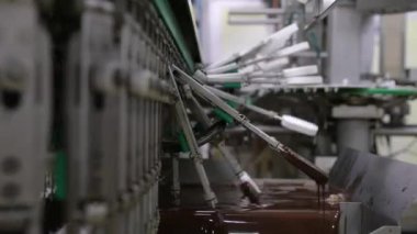 Sanayi dondurma fabrikası. Gıda üretim sektöründe otomasyon ve teknoloji. Çikolataya kremalı dondurma taşıyıp batıran bir makine görüntüsü.