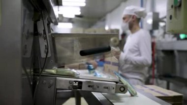 Gıda endüstrisi ve teknoloji. Dondurmaları plastik bir paketle paketleyen ticari ambalaj makinesinin yakın görüntüsü. Fabrika işçileri ürünleri arka planda boks yapıyor.