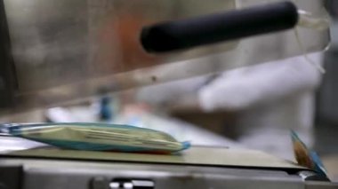 Gıda endüstrisi ve teknoloji. Dondurmaları plastik bir paketle paketleyen ticari ambalaj makinesinin yakın görüntüsü. Fabrika işçileri ürünleri arka planda boks yapıyor.