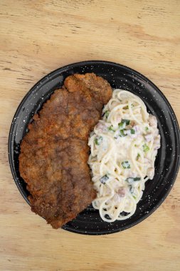 Makarna ve et. Milanesa 'nın en iyi manzarası, ekmek arası biftek, ve domuz pastırması ve pırasa kremalı spagetti, restoranın ahşap masasında siyah bir tabakta.. 