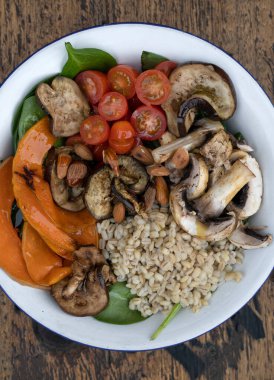 Izgara sebzeli besleyici salatanın en iyi görüntüsü. Izgara balkabağı, mantar, ıspanak, arpa, badem ve kiraz domatesli vejetaryen salatası. Restoranın ahşap masasında beyaz bir kasede..