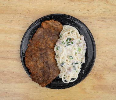 Makarna ve et. Milanesa 'nın en iyi manzarası, ekmek arası biftek, ve domuz pastırması ve pırasa kremalı spagetti, restoranın ahşap masasında siyah bir tabakta.. 