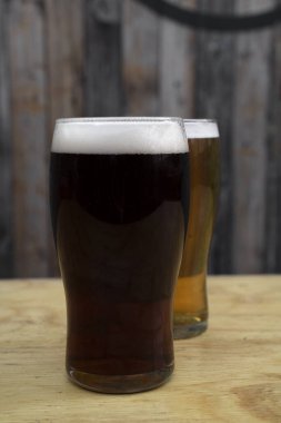 İki bardak bira, ballı altın bir bira ve siyah, ahşap arka planı olan bir bira.