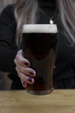 İçkiler. Barda elinde bir bardak siyah bira tutan beyaz bir kadının yakın görüntüsü..