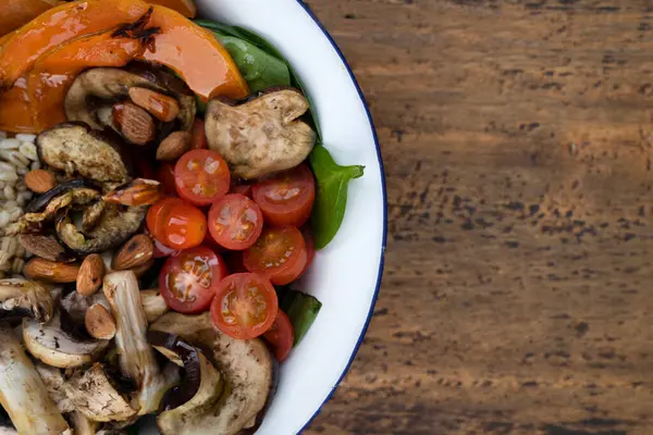 Izgara sebzeli besleyici salatanın en iyi görüntüsü. Izgara balkabağı, mantar, ıspanak, arpa, badem ve kiraz domatesli vejetaryen salatası. Restoranın ahşap masasında beyaz bir kasede..