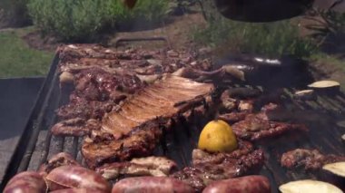 Barbekü dışarıda. Eti, pirzolaları ve demir ızgarada fırçayla fırçalayan erkek eli yakından görülüyor..