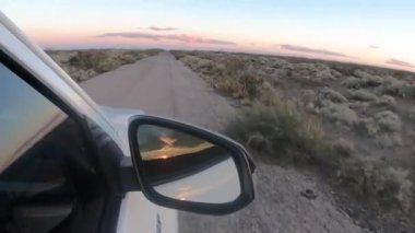 Alacakaranlıkta çöl yolunda seyahat ediyorum. 4x4 'lük bir aracın toprak yolda giderken görüntüsü. Yan aynadaki manzara yansıması..