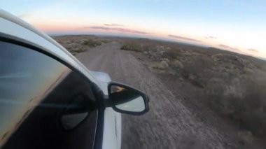 Alacakaranlıkta çöl yolunda seyahat ediyorum. 4x4 'lük bir aracın toprak yolda giderken görüntüsü. Yan aynadaki manzara yansıması..