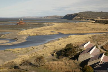 Seascape. View of the ocean, beach and coastal yellow meadow in a sunny day in San Pablo Cape, Tierra del Fuego, Argentina. An old historical shipwreck called Desdemona in the sand. clipart