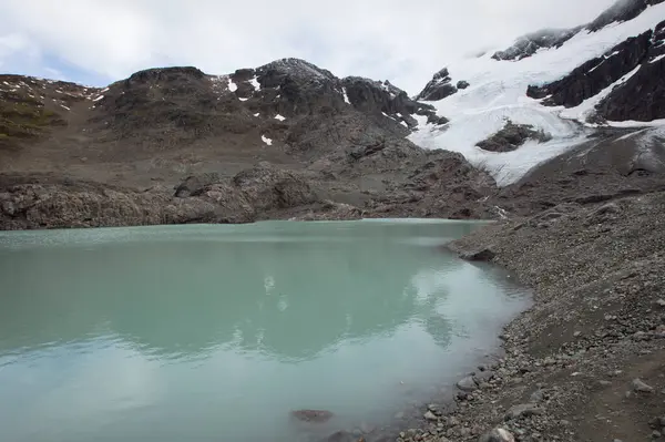 Alp arka planı. Cordillera 'da yüksek buzul suyu gölü. Turkuaz renkli gölün kayalık dağın tepesindeki görüntüsü ve karlı zirvede Buzul Vinciguerra.. 