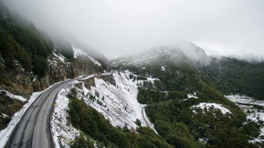 Paso Garibaldi otoyolunun havadan görüntüsü. Seyahat et. Tierra del Fuego, Patagonya Arjantin 'deki kar, sis, dağlar ve çam ağaçları arasında 3. yol. Alplere giden yol.