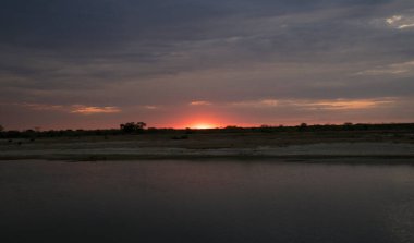 Dramatik gün batımı. Nehrin uzun pozlu görüntüsü, ufukta çöl ve güneş gizleniyor. Güzel alacakaranlık ışığı ve bulanık su efekti.