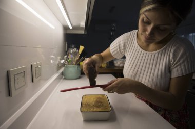 Genç yetişkin bir kadın evinde yemek pişiriyor. Sıcak manzaralı kız Tiramisu tatlısı üzerine çikolata rendeliyor..
