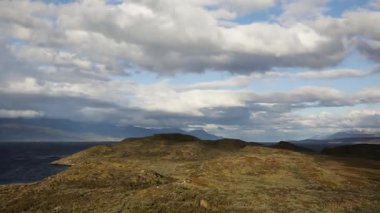 Idyllic manzara. Adanın sarı çayır manzarası ve bulutlu görkemli gökyüzünün altındaki tepeler. Arka planda Beagle Kanalı okyanusu