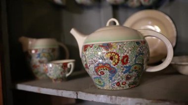 Sanatsal bulaşık takımı antikaları. Porselen bir çaydanlık ve çay fincanı setinin yakın görüntüsü, renkli çizimlerle.