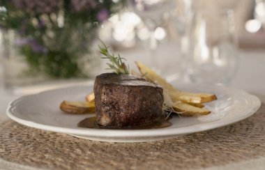 Gurme gastronomi. Düğün ana yemeği. Yakından bakınca kırmızı şarap soslu ızgara fileto ve masada güzel bir cam eşyalar ve sofra takımı ile patates.