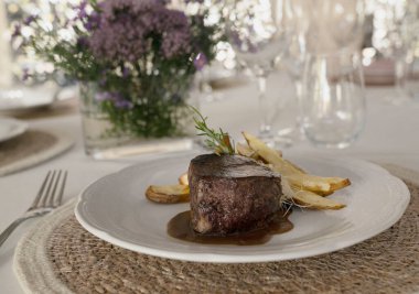 Gurme gastronomi. Düğün ana yemeği. Yakından bakınca kırmızı şarap soslu ızgara fileto ve masada güzel bir cam eşyalar ve sofra takımı ile patates.